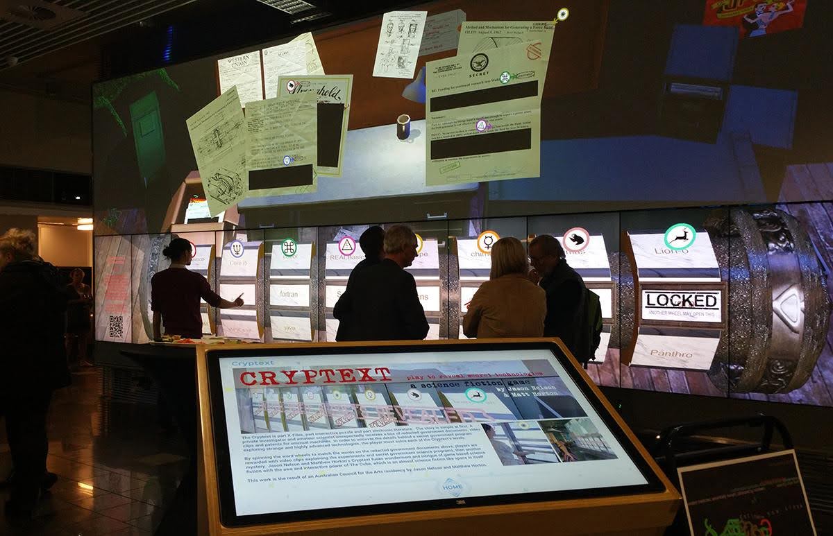 People stand in front of a large screen. On the screen you can
                                        see old documents and a large locking mechanism. There is a podium visible as well, with a line of text that reads cryptext.