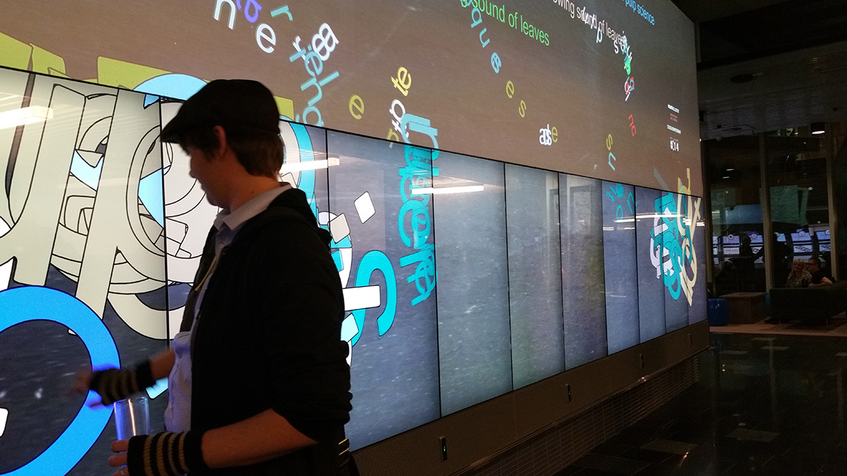 An image of a person interacting with a large touch-screen. On the screen you can
                                        see colorful letters.